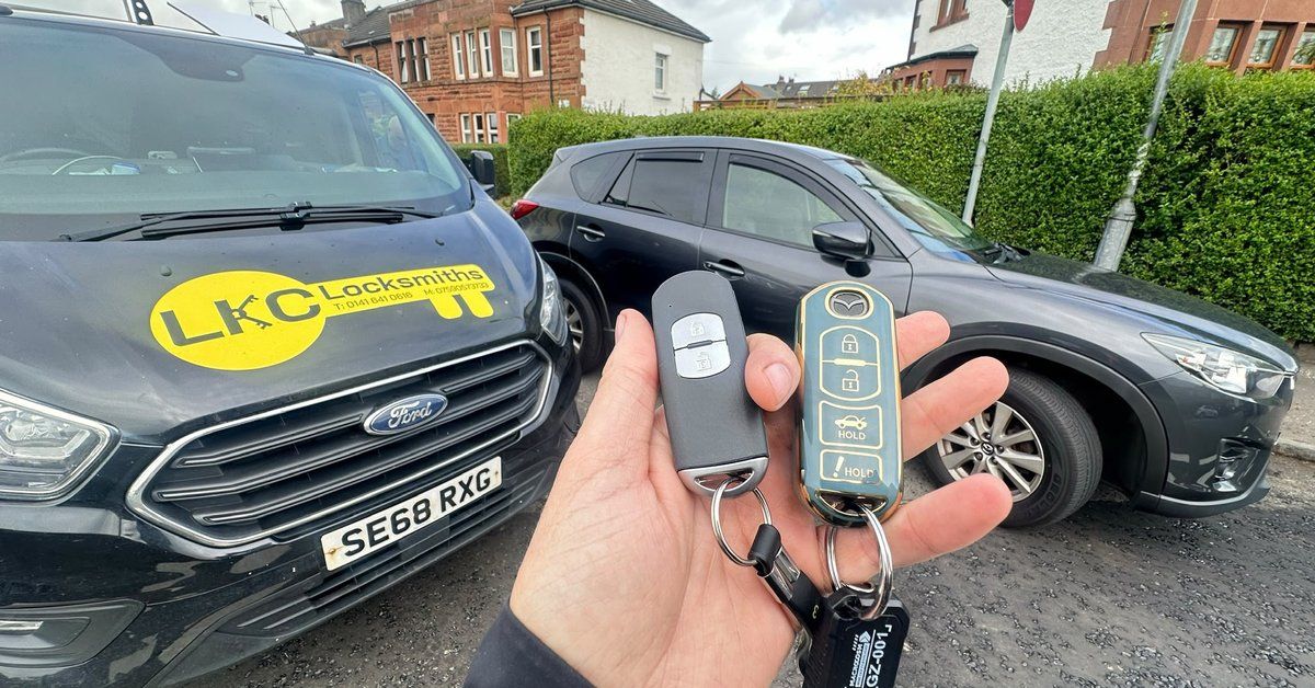 Two Mazda car keys held beside the branded LKC Locksmiths van